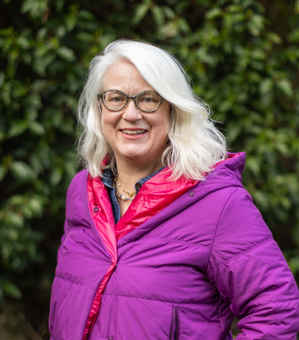 Portrait of Heather Eberhardt wearing a purple jacket and glasses, smiling outdoors.