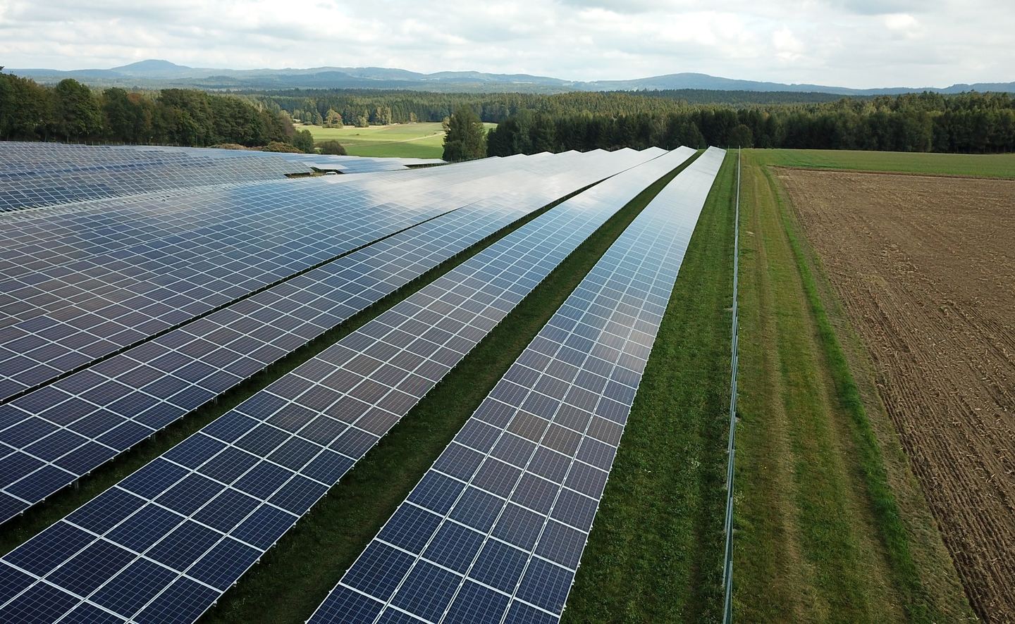 Aerial view of solar panels in a field with a car and tractor driving between them.